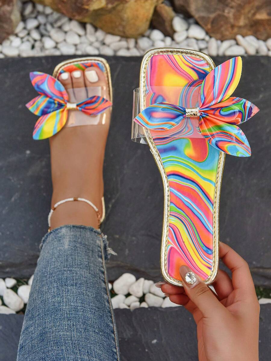 Rainbow swirl bow slide sandal worn on foot with metallic gold trim