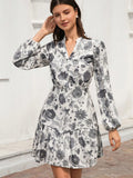 A woman wearing a long-sleeve white dress with a gray and black floral print, standing against a white stucco wall.