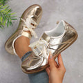 Front three-quarter view of metallic gold ribbon-lace sneaker with gum sole