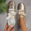 Top-down view of metallic gold low-top sneakers with white satin ribbon laces