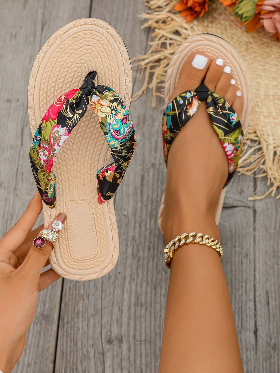 Overhead beige and black floral flip-flops shown worn and held on wood