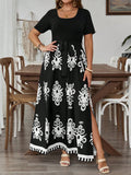 A woman models a black short-sleeve maxi dress with a white Mexican-style floral pattern and a side slit, standing in a dining room setting.