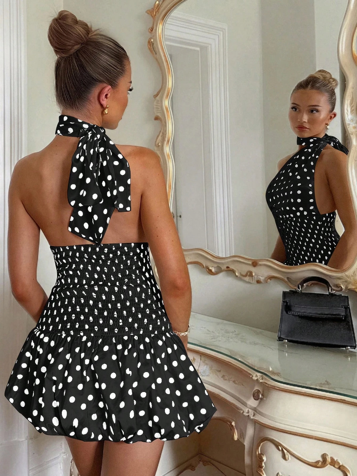 Woman wearing a black polka dot dress in front of a mirror.