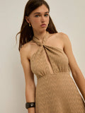 A woman wearing a halter-neck dress with a wavy textured pattern in a warm tan/beige color, posed against a plain light gray background.
