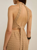 A woman shown from the back wearing a beige knit dress with a wavy pattern and an open back tied at the waist, photographed against a plain light background.