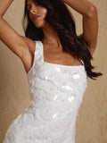 A woman wearing a white textured sleeveless dress with sequined details, posed against a warm beige background.