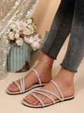 Gold flat sandals with diagonal rhinestone straps and metallic footbed