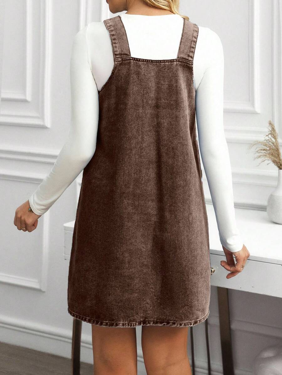 Back view of coffee brown denim pinafore dress showing broad straps and clean mini hem