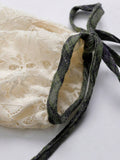 Close-up of gathered ivory lace dress sleeve cuff with green plaid tie bow