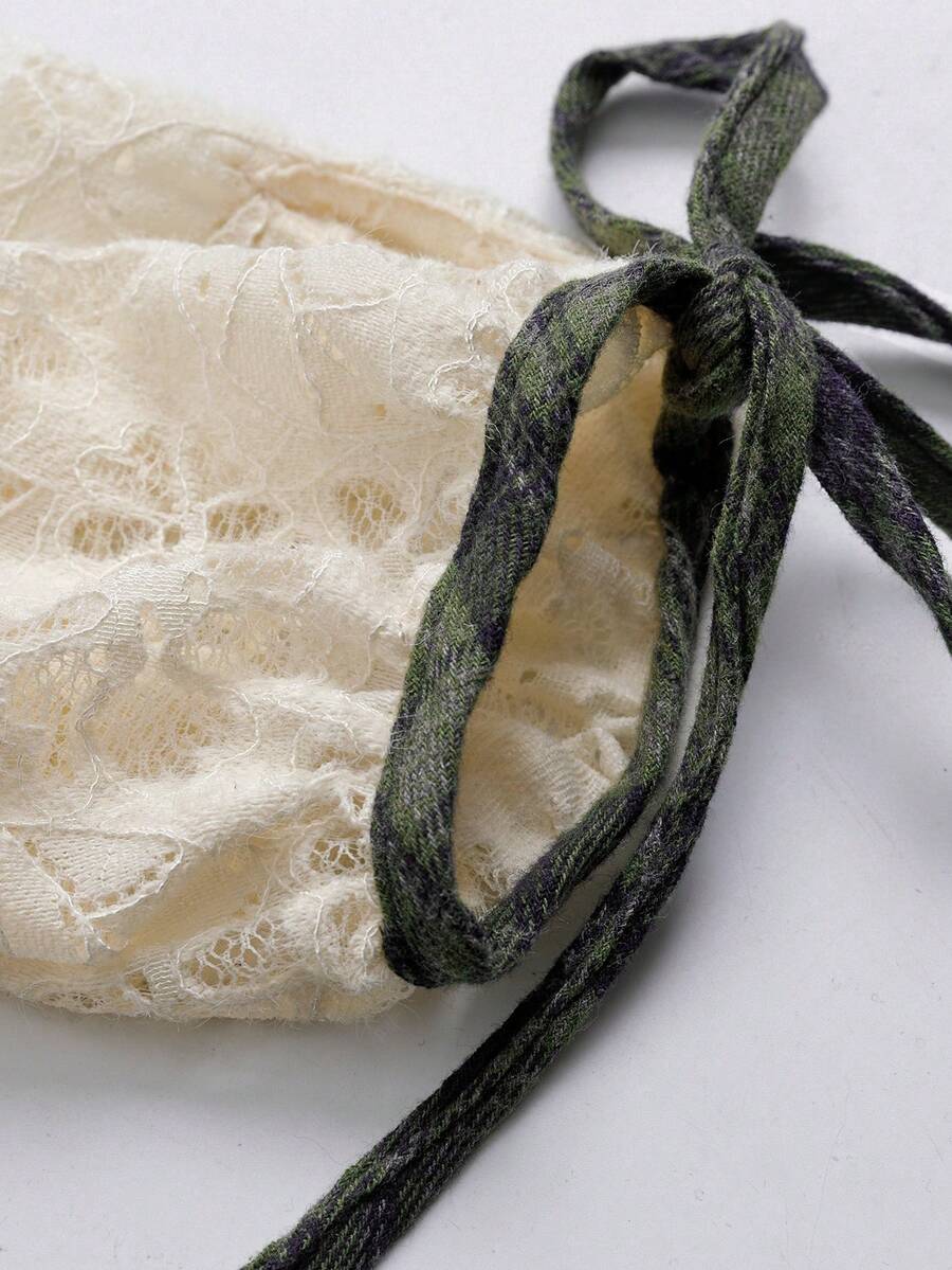 Close-up of gathered ivory lace dress sleeve cuff with green plaid tie bow