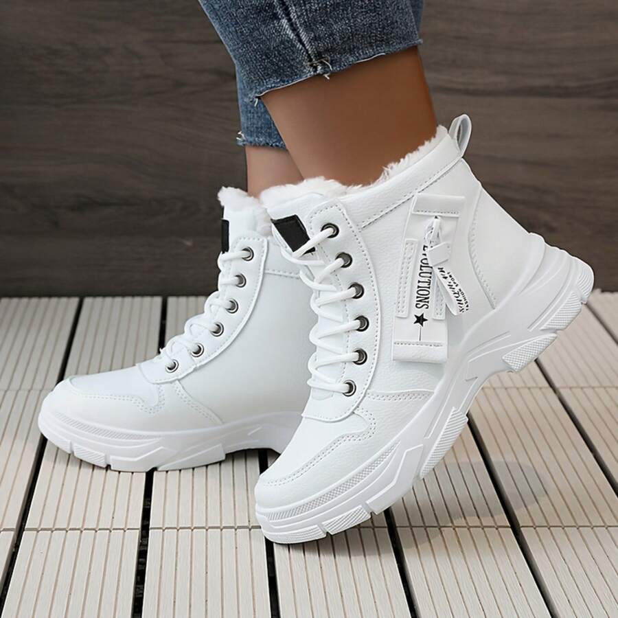 Side front view of white winter combat boots worn with jeans on wooden decking