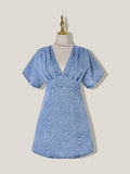 Front view of light-wash A-line denim mini dress with V neckline and curved stitched hem