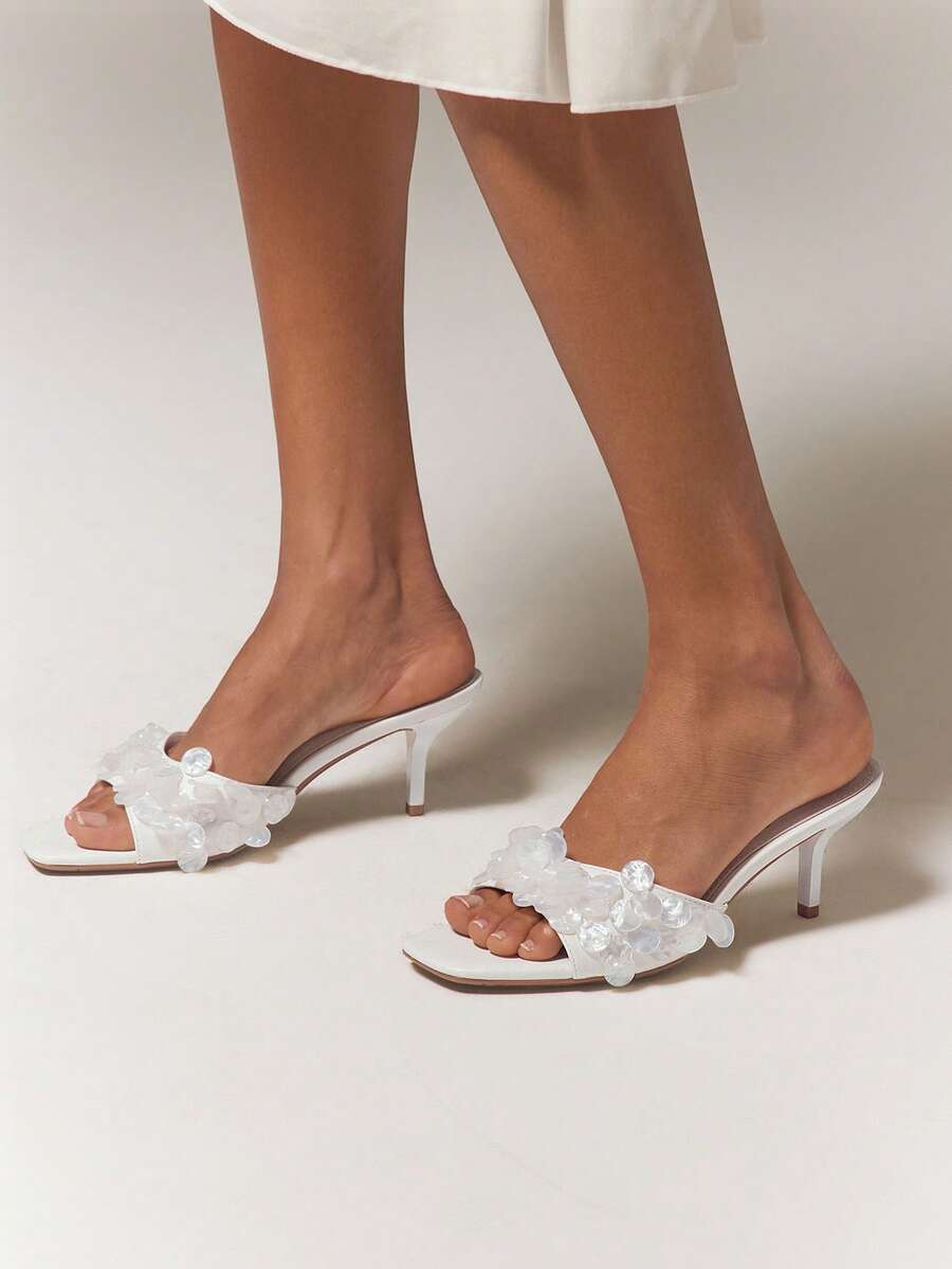 Worn front view of white embellished kitten-heel mules with clear layered vamp details