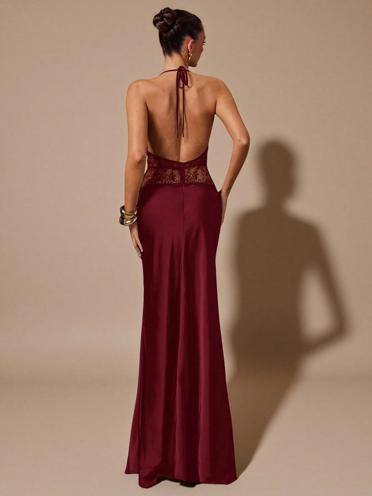 Woman wearing a burgundy evening gown with a lace back on a beige background
