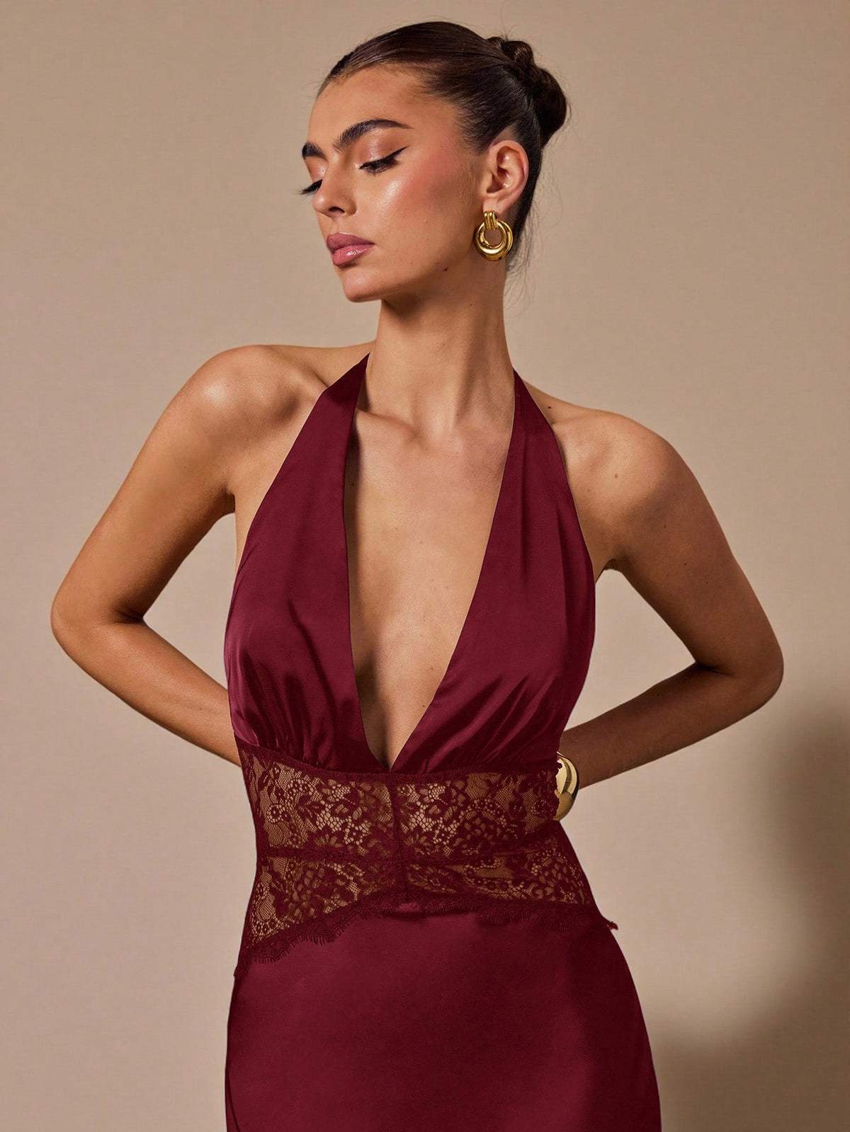 Woman wearing a burgundy halter neck dress with lace detail on a beige background