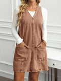 Full front view of mocha brown denim pinafore mini dress with deep V neck and utility pockets