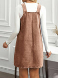 Back view of mocha brown denim pinafore dress showing broad straps and relaxed mini shape