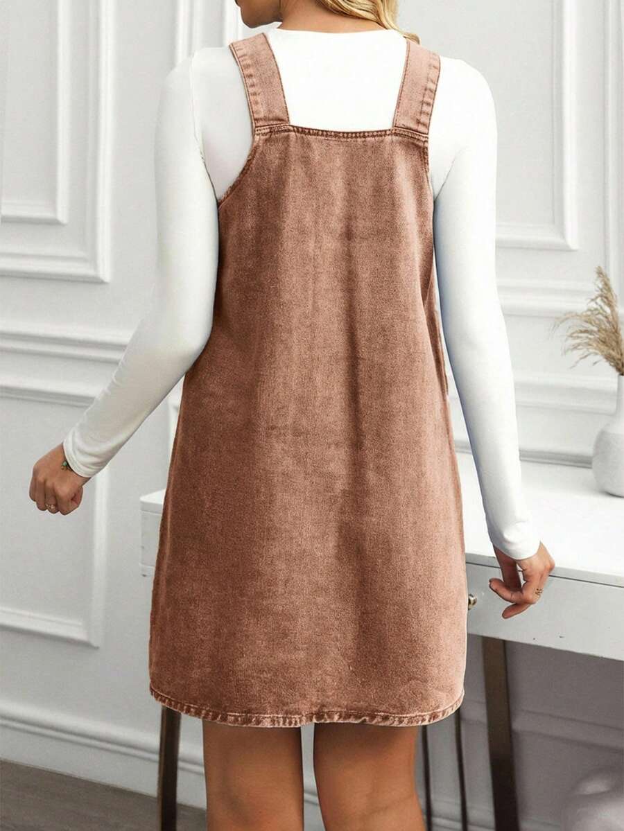 Back view of mocha brown denim pinafore dress showing broad straps and relaxed mini shape