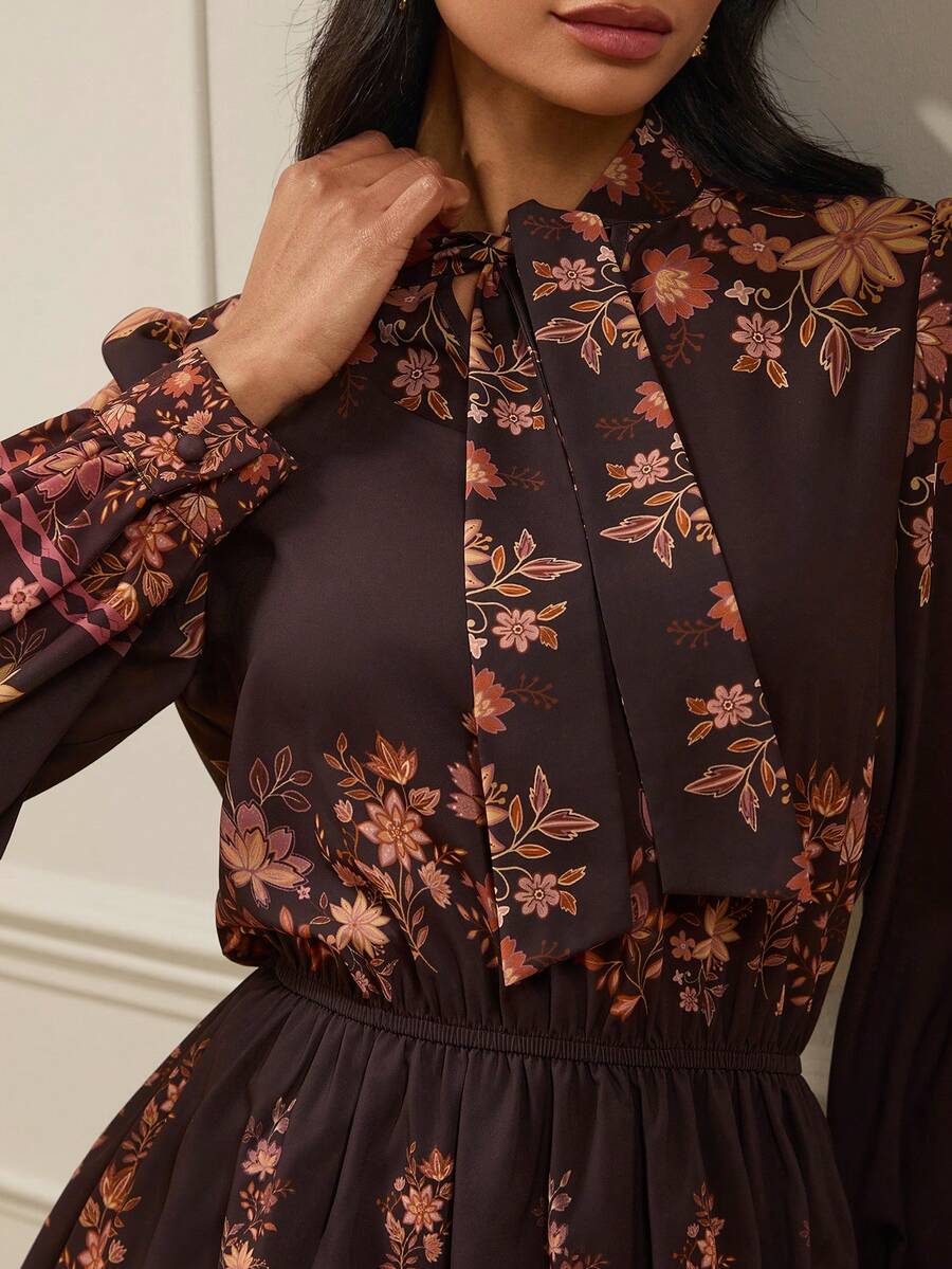 Embrace the warmth of the seasons with this elegant floral print dress, a versatile earth-tone essential designed for seamless transitions between spring and autumn. Featuring a sophisticated tie collar and graceful lantern sleeves, this piece perfectly captures a refined, vintage-inspired aesthetic. The delicate botanical patterns in rich, muted tones offer a timeless appeal that complements any landscape, while the lightweight, high-quality fabric ensures a comfortable and flattering flow. Whether paired 