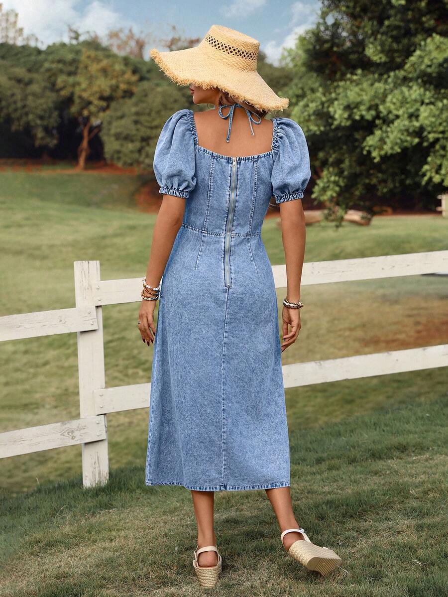 Front three-quarter view of blue acid-wash denim midi dress with puff sleeves and fitted waist in a garden