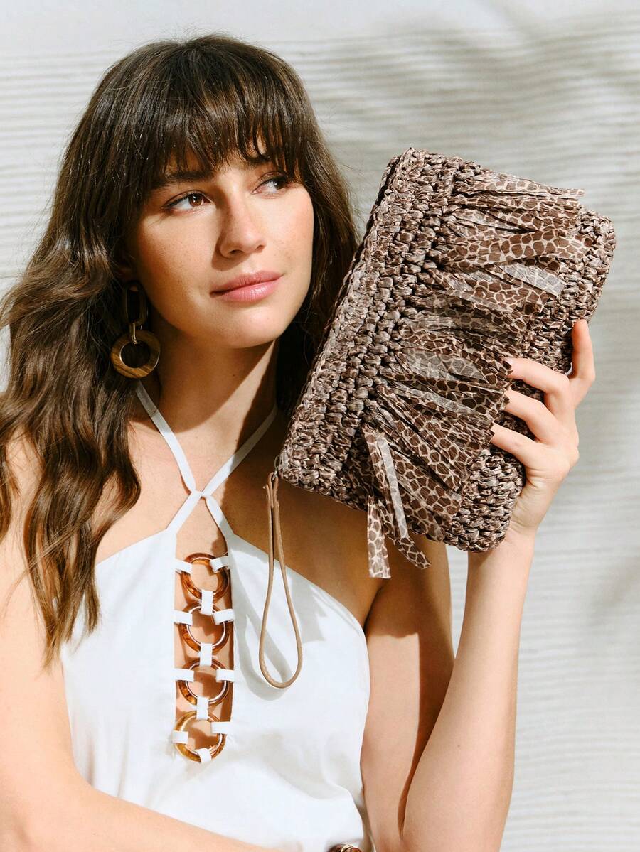 Woman holding brown woven animal print tassel clutch bag with wristlet strap while wearing white halter top with ring details