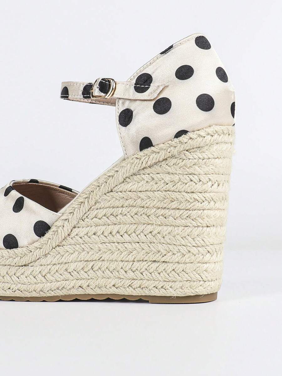 Side close-up of ivory and black polka-dot espadrille wedges with braided rope platform and ankle strap