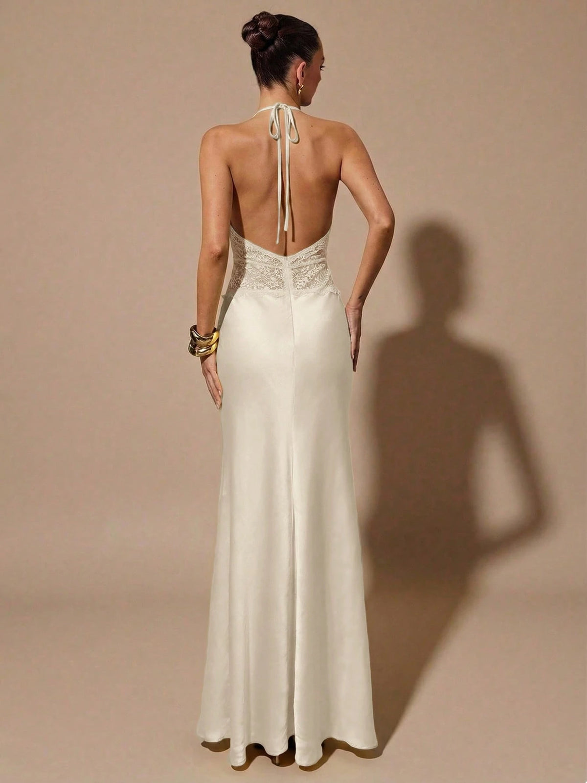 Woman wearing a white evening gown with a backless design on a beige background