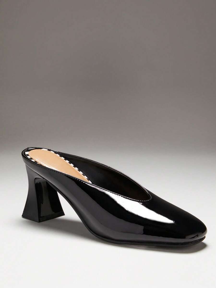 Black side profile view of patent mule pumps with closed vamp, open back, softly squared toe, and flared block heel