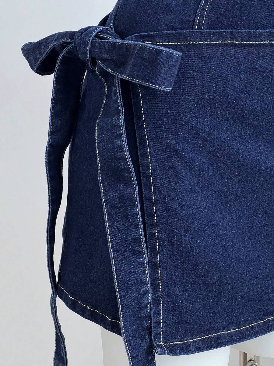 Close-up of dark indigo denim mini dress side bow, long waist ties, stitched seam, and mini hem