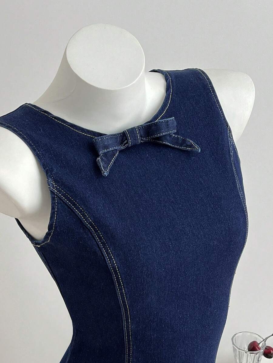 Close-up front view of dark indigo sleeveless denim dress with round neck bow and shaped bodice seams