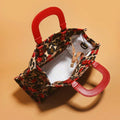 Overhead view of open cherry and leopard-print handbag showing pale interior, zipper and red handles