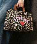 Handheld leopard-print handbag with pink LOVE ME lettering and red heart styled beside blue denim