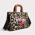 Three-quarter view of leopard-print handbag with pink LOVE ME lettering, red heart and brown handles