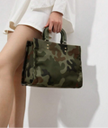 Handheld green camouflage square handbag with olive handles styled against a white outfit