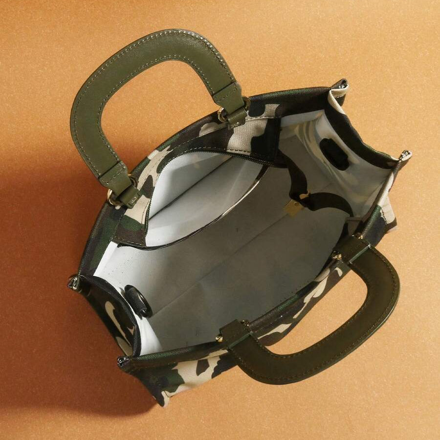 Overhead view into green and cream camouflage handbag showing pale interior and open zipper