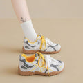 Side view of white, gray, and yellow lace-up sneaker worn with textured gum sole