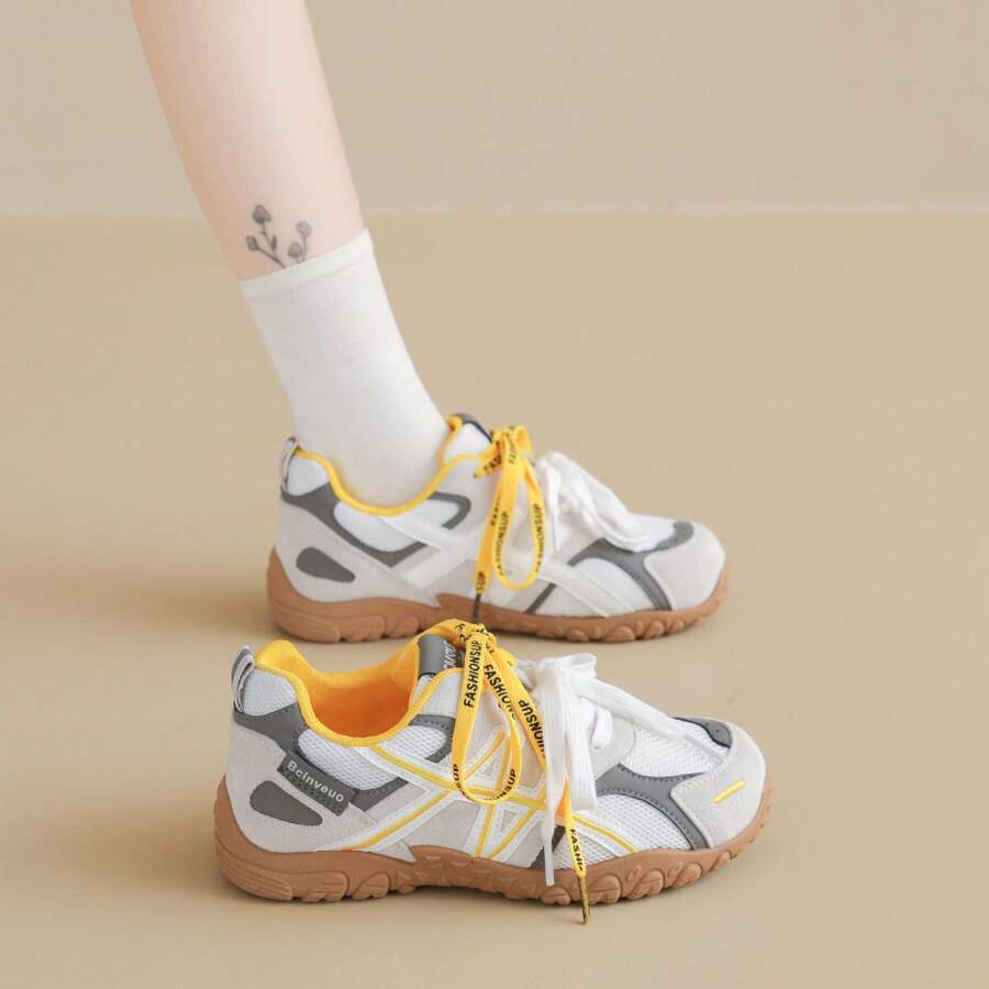 Side view of white, gray, and yellow lace-up sneaker worn with textured gum sole