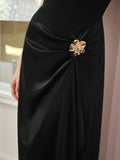 Close-up of black dress showing gathered waist, lustrous drape, and gold floral ornament