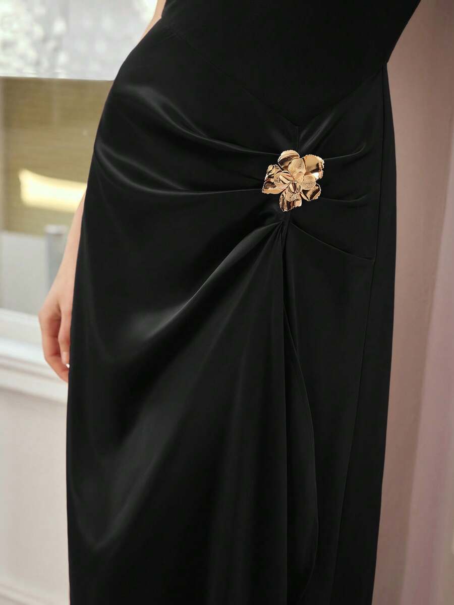 Close-up of black dress showing gathered waist, lustrous drape, and gold floral ornament