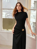 Front three-quarter view of black draped evening dress with gold hip flower and asymmetric panel