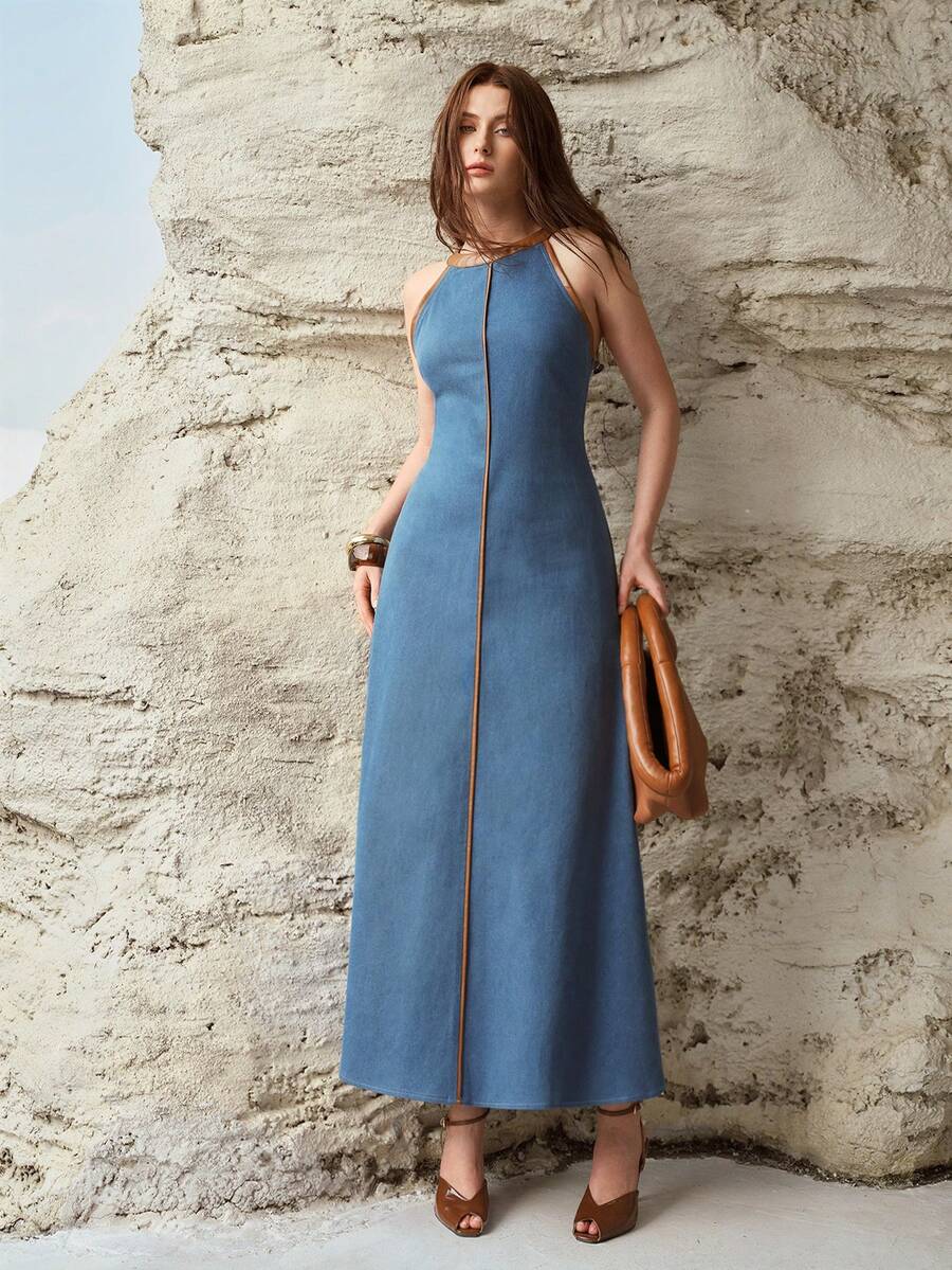 Front three-quarter view of medium blue contrast trim halter denim maxi dress by a rock wall