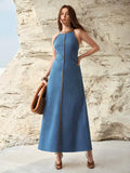 Front three-quarter view of medium blue contrast trim halter denim maxi dress by a rock wall