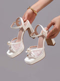 Pair of white platform sandals held in hands with lace panels and pearl bows