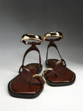 Pair of brown flat thong sandals with curved gold-tone toe and ankle cuffs
