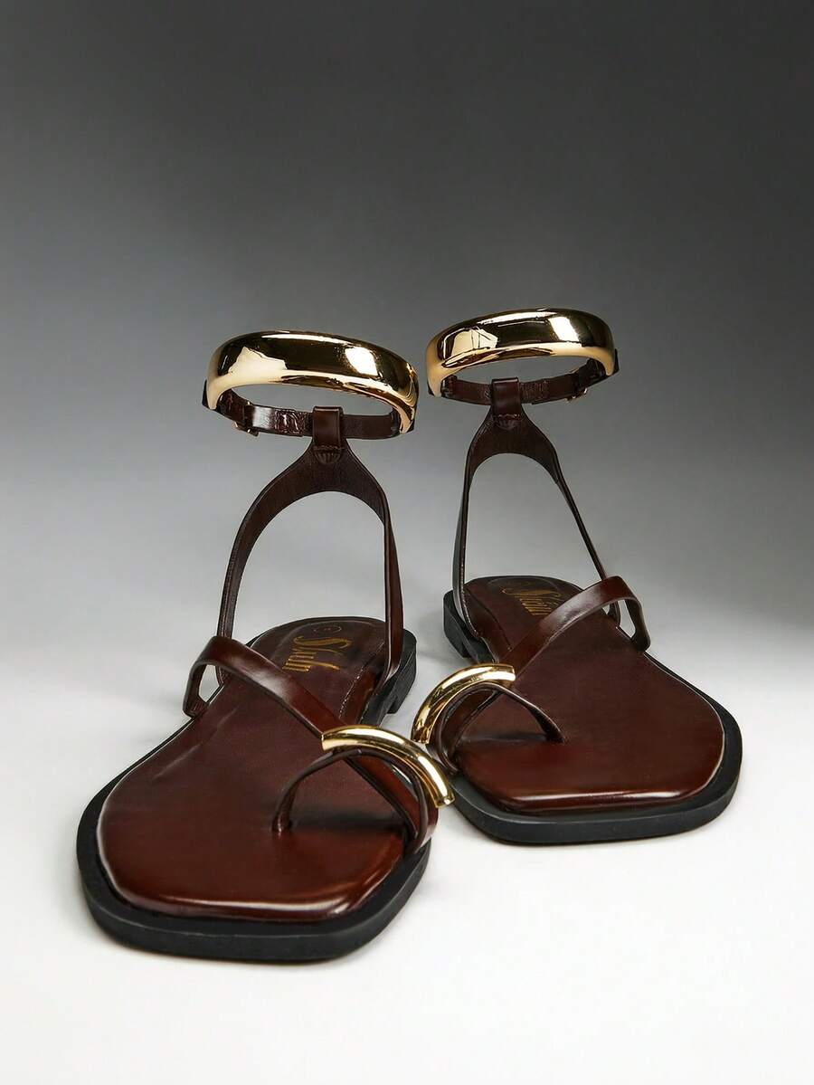 Pair of brown flat thong sandals with curved gold-tone toe and ankle cuffs