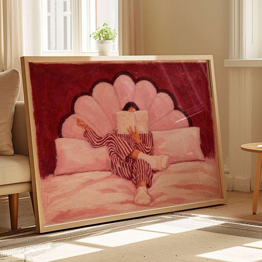 Angled floor display of pink reading woman artwork in a cream frame by a chair