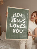 Held portrait view of sage green Jesus Loves You canvas print in white frame