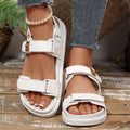 Front three-quarter view of white open toe platform sandals worn on a wood floor