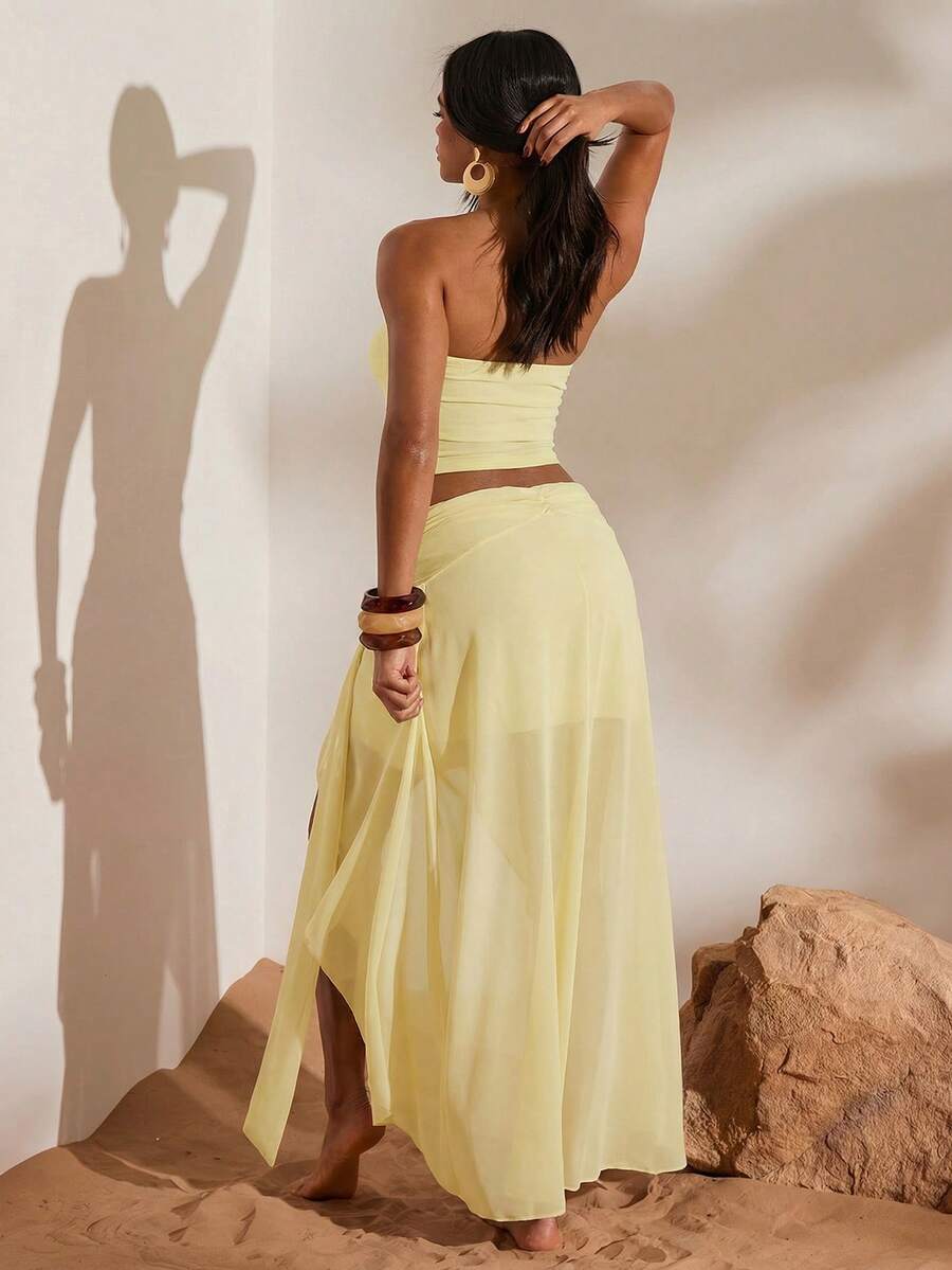 Back view of light yellow mesh bandeau crop top and flowing high-slit maxi skirt two-piece set for beach vacation styling