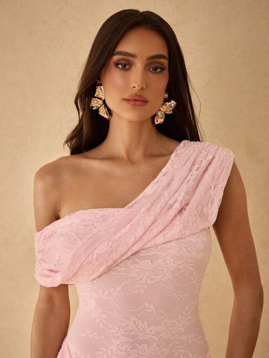 View 1 of baby pink lace one shoulder maxi dress with asymmetric neckline, draped overlay, fitted bodice, and sheer skirt